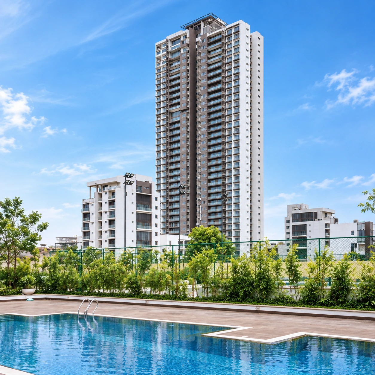 Exterior view of a tall, modern luxury high-rise residential tower featuring a clear swimming pool and landscaped gardens on a sunny day in Gurgaon.